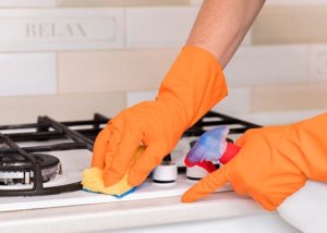 A person wearing orange gloves cleaning a kitchen with a cloth and cleaning spray