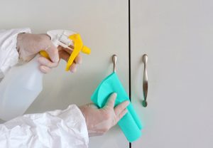 A man cleaning a wardrobe with a towel and spray while wearing gloves