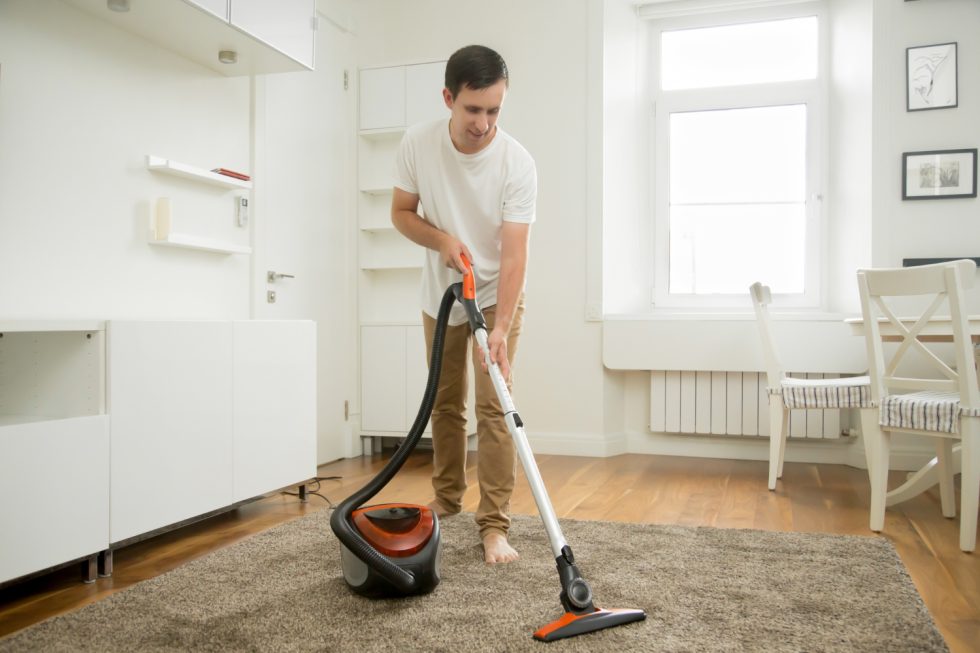 A man using a carpet cleaning machine to clean a carpet with a smile on his face